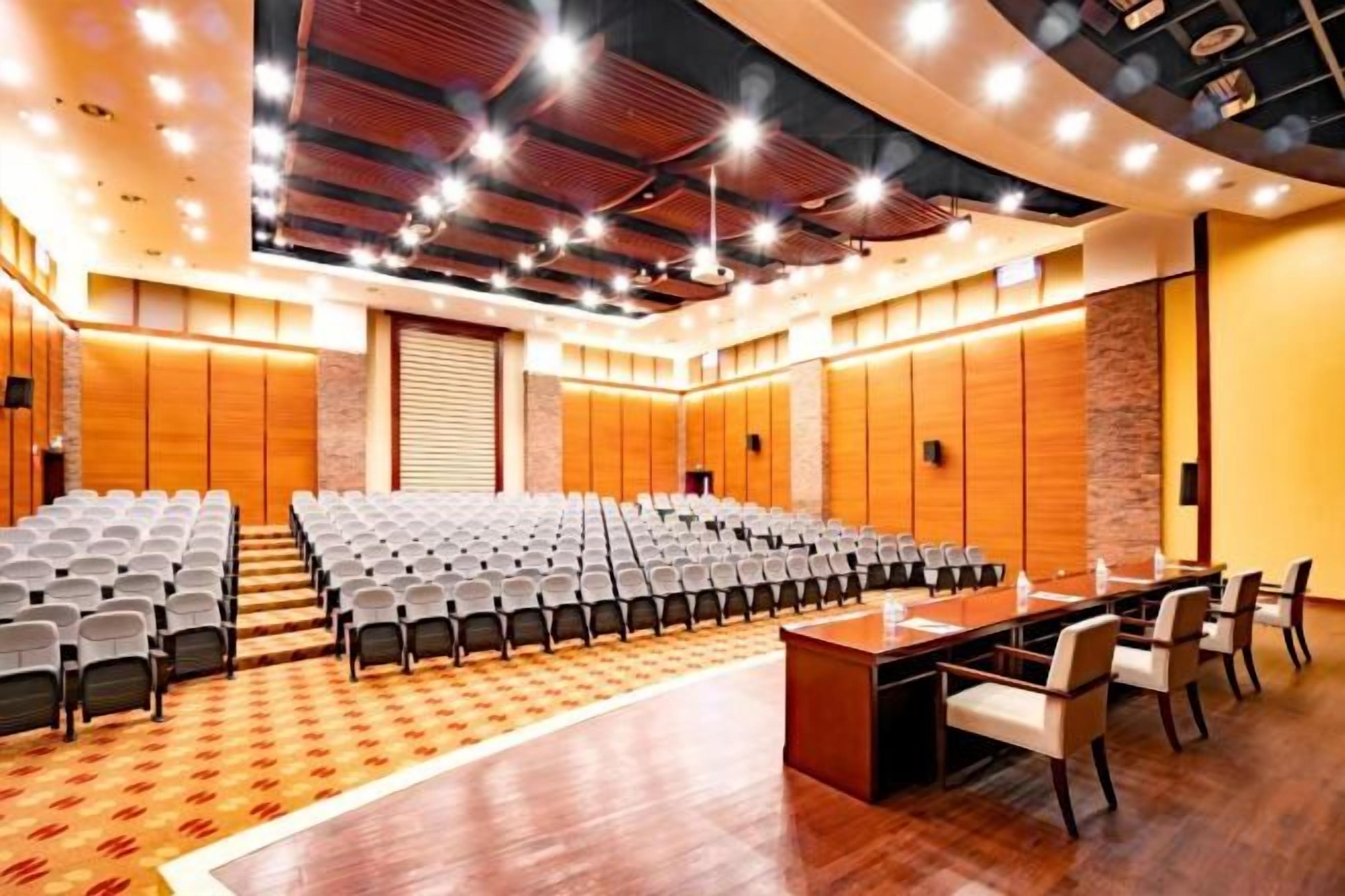 A conference room with rows of chairs, a long table, and a stage.
