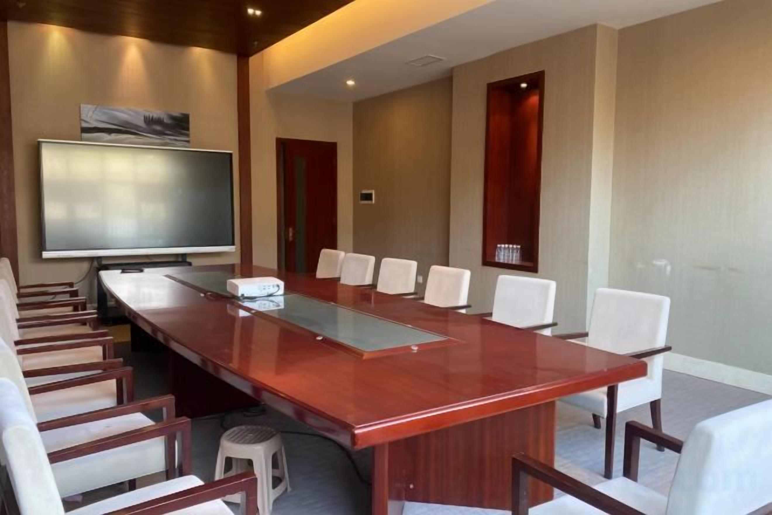 A conference room with a long table, white chairs, a flat-screen TV, and a projector.