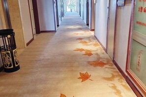 A hotel corridor with a carpet featuring autumn leaves, a trash bin, and a wall with a framed item. - Maple Palace Hotel (Kunming)