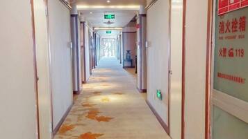 A hotel corridor with doors on both sides, a carpet with leaf patterns, and a fire hydrant box sign on the right wall.