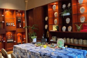 Un coin repas avec une table dressée pour deux personnes, entouré d’étagères remplies de bouteilles et d’assiettes.