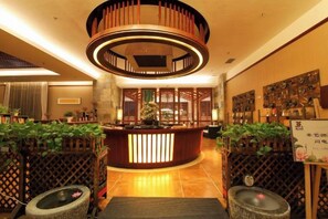 A reception area with a circular wooden structure, a reception desk, and potted plants. - Maple Palace Hotel (Kunming)