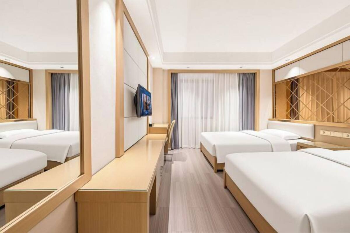 A hotel room with two beds, a TV, a desk, and a mirror.