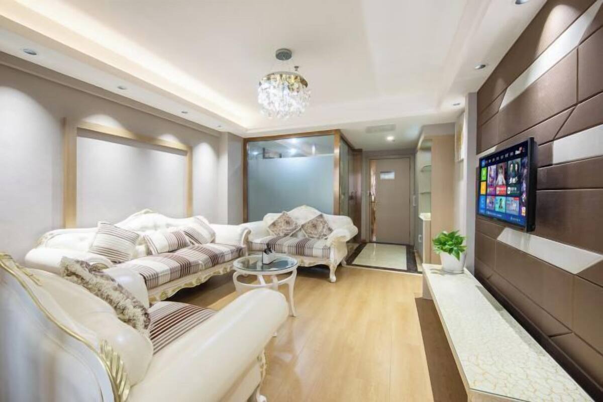 A modern living room with a sofa set, a coffee table, a TV mounted on the wall, and a chandelier.