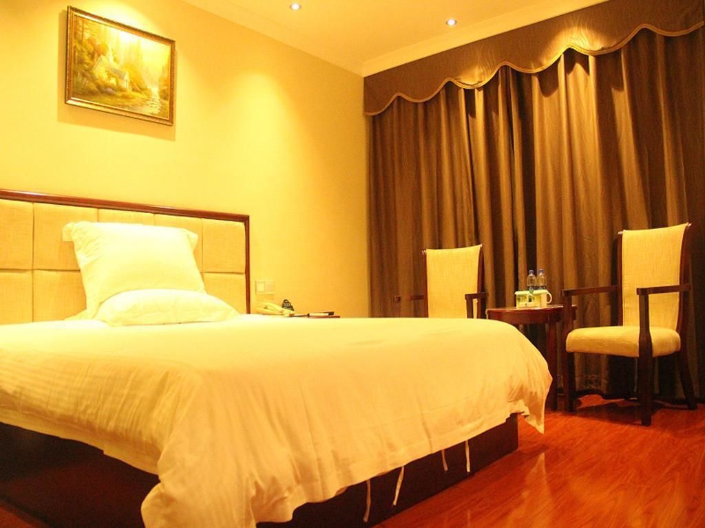 A hotel room with a large bed, two chairs, a small table with a bottle, and a painting on the wall.