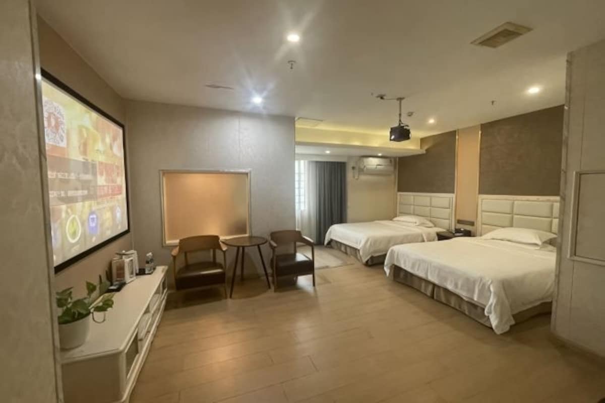 A hotel room with two beds, a desk, and a TV screen.