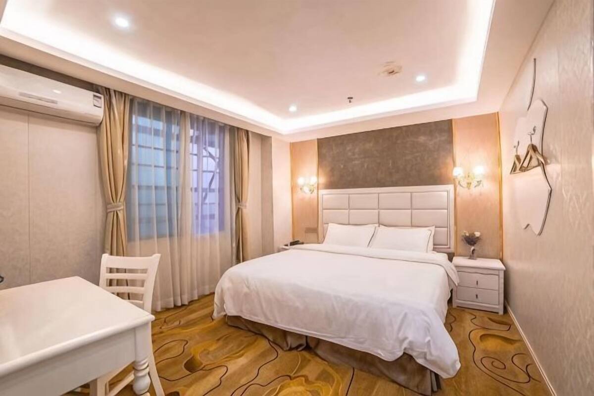 A hotel room with a bed, bedside table, chair, and a desk.