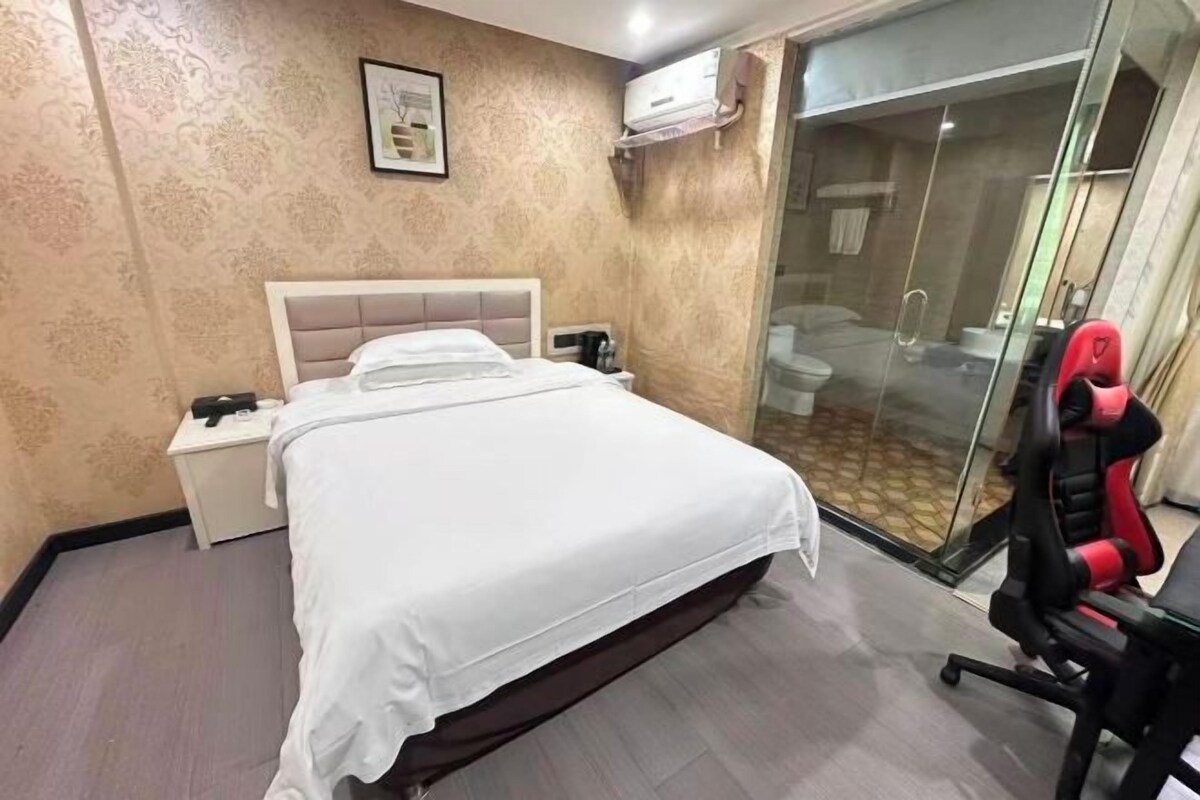 Habitación de hotel con cama, mesita de noche y cabina de ducha de vidrio.