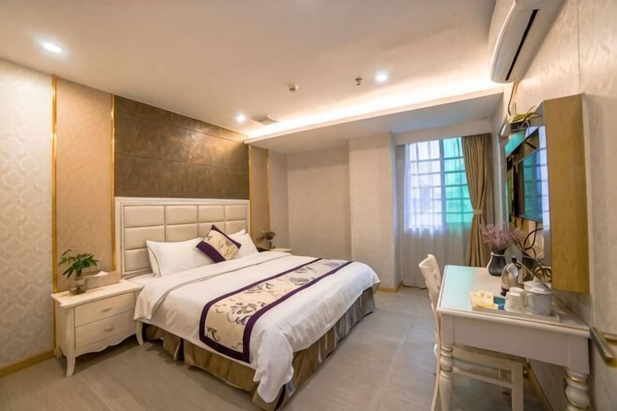 A bedroom with a bed, bedside table, nightstand, desk, chair, and a mirror.