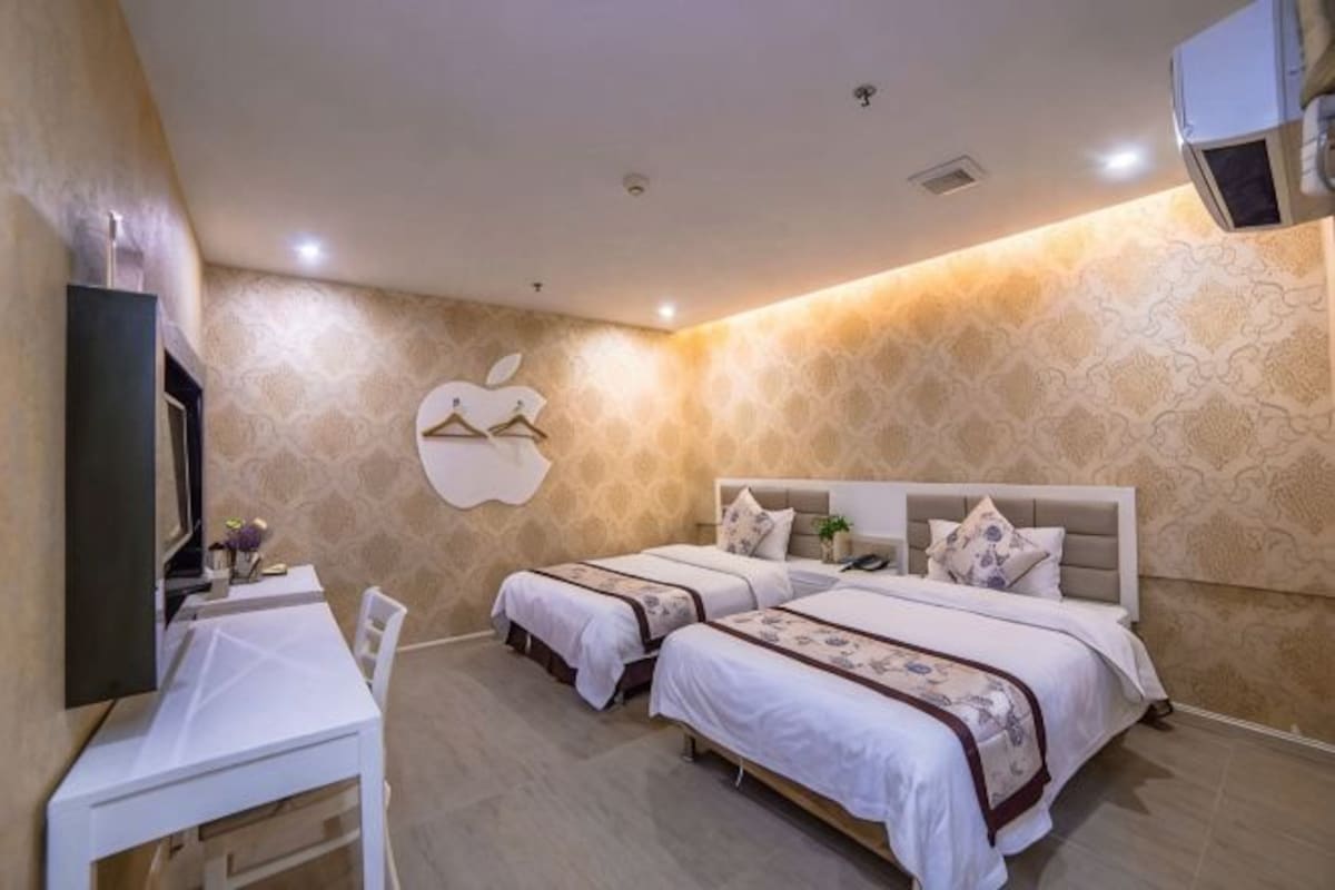 A hotel room with two beds, a desk, and a TV.