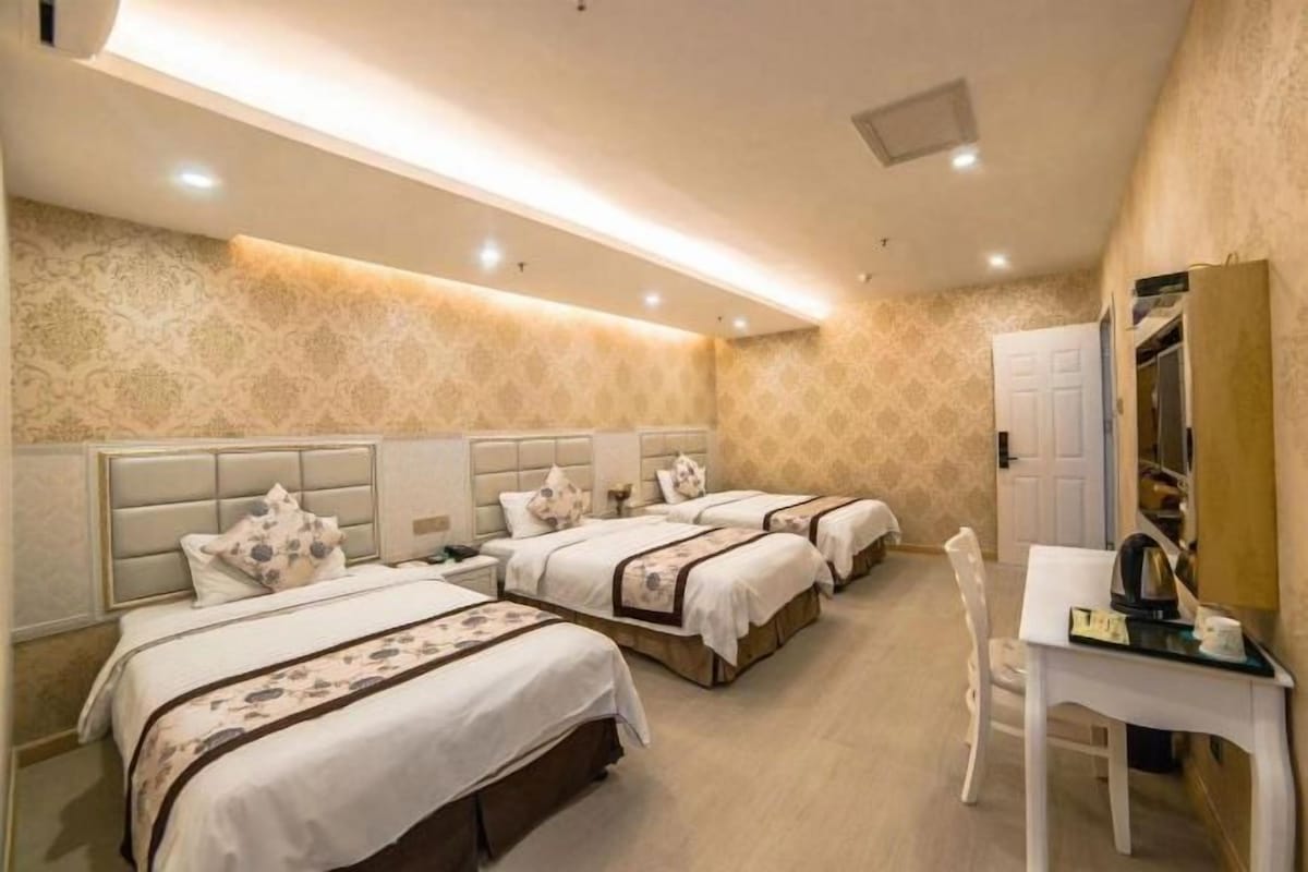 A hotel room with three beds, a desk, and a chair.