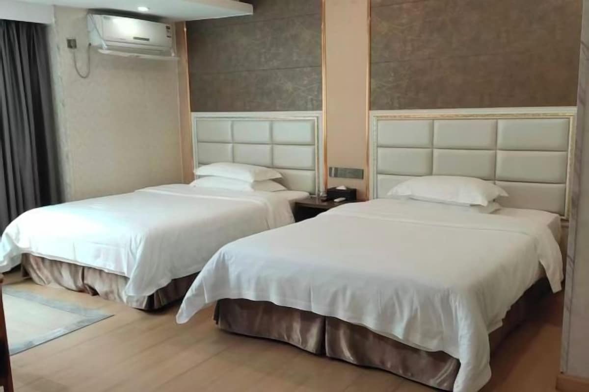 A hotel room with two beds, a nightstand, and an air conditioning unit.