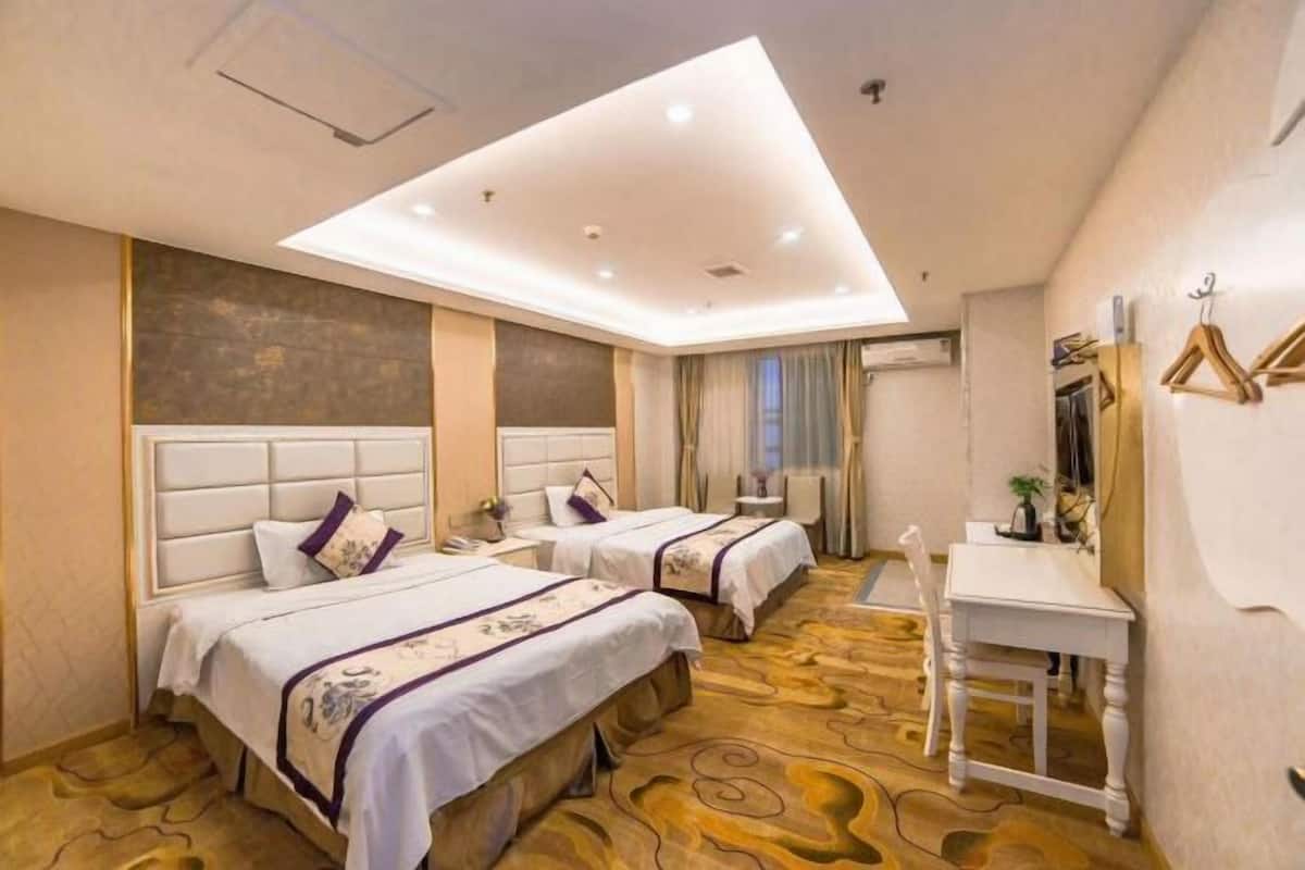 A hotel room with two beds, a desk, a chair, and a large window.