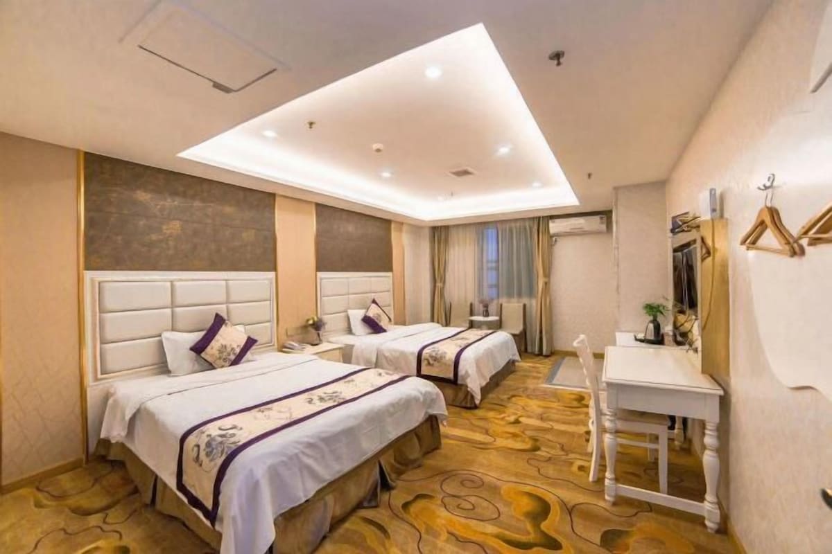 A hotel room with two beds, a desk, a chair, and a large window.