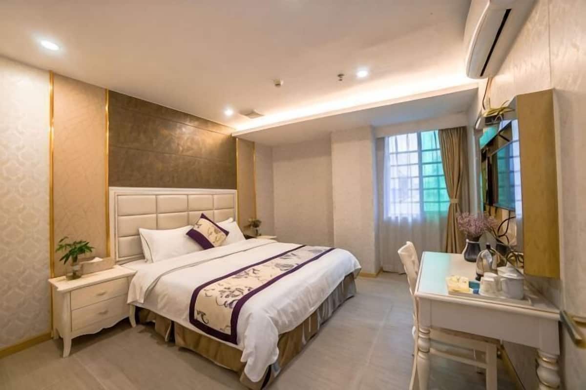 A bedroom with a bed, bedside table, nightstand, desk, chair, and a mirror.