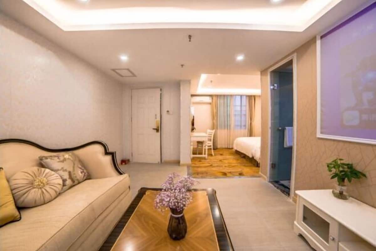 A hotel room with a sofa, a coffee table with a vase, a TV, a bed, and a bathroom visible through an open door.