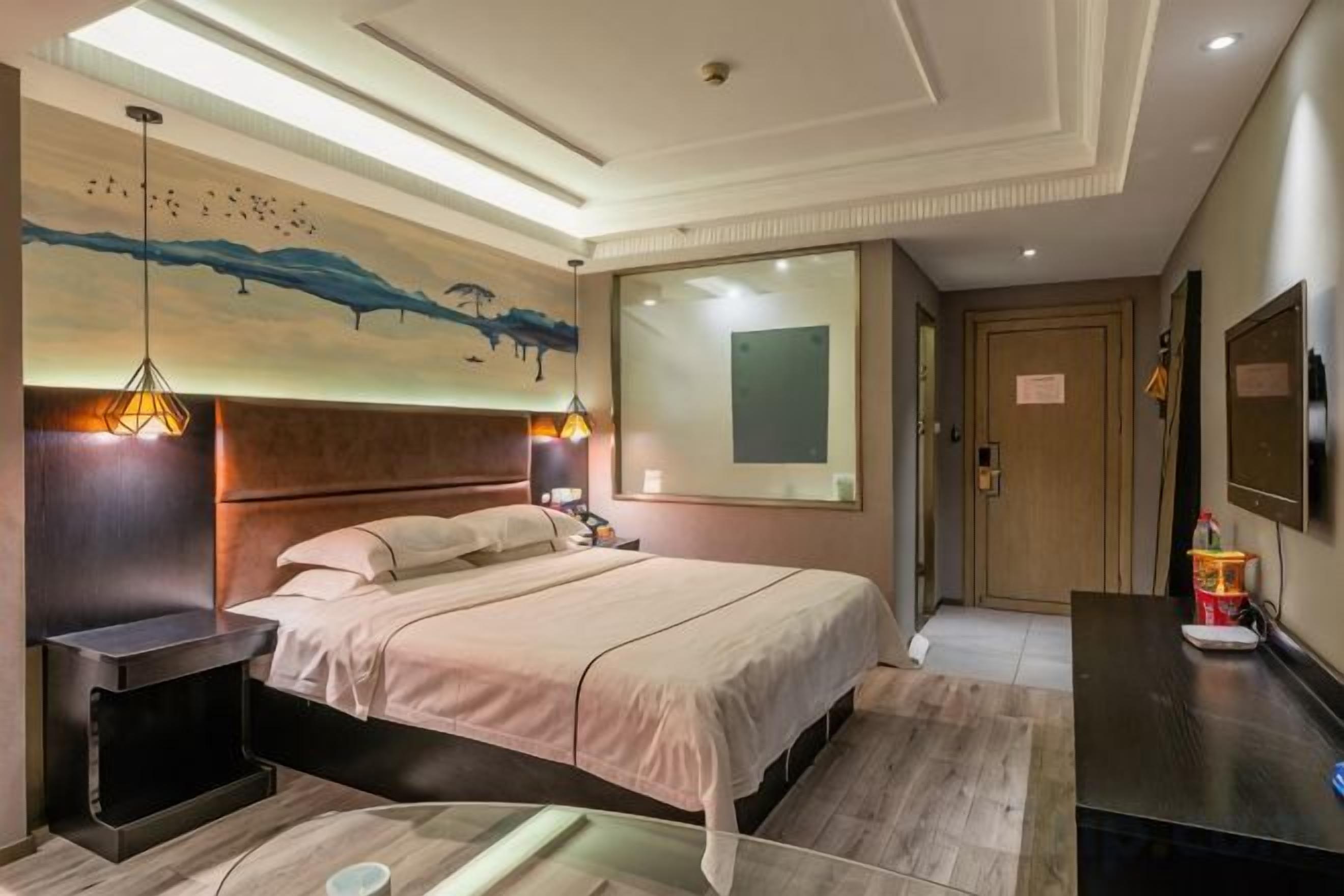A hotel room with a bed, bedside tables, a desk, a mirror, and a painting on the wall.