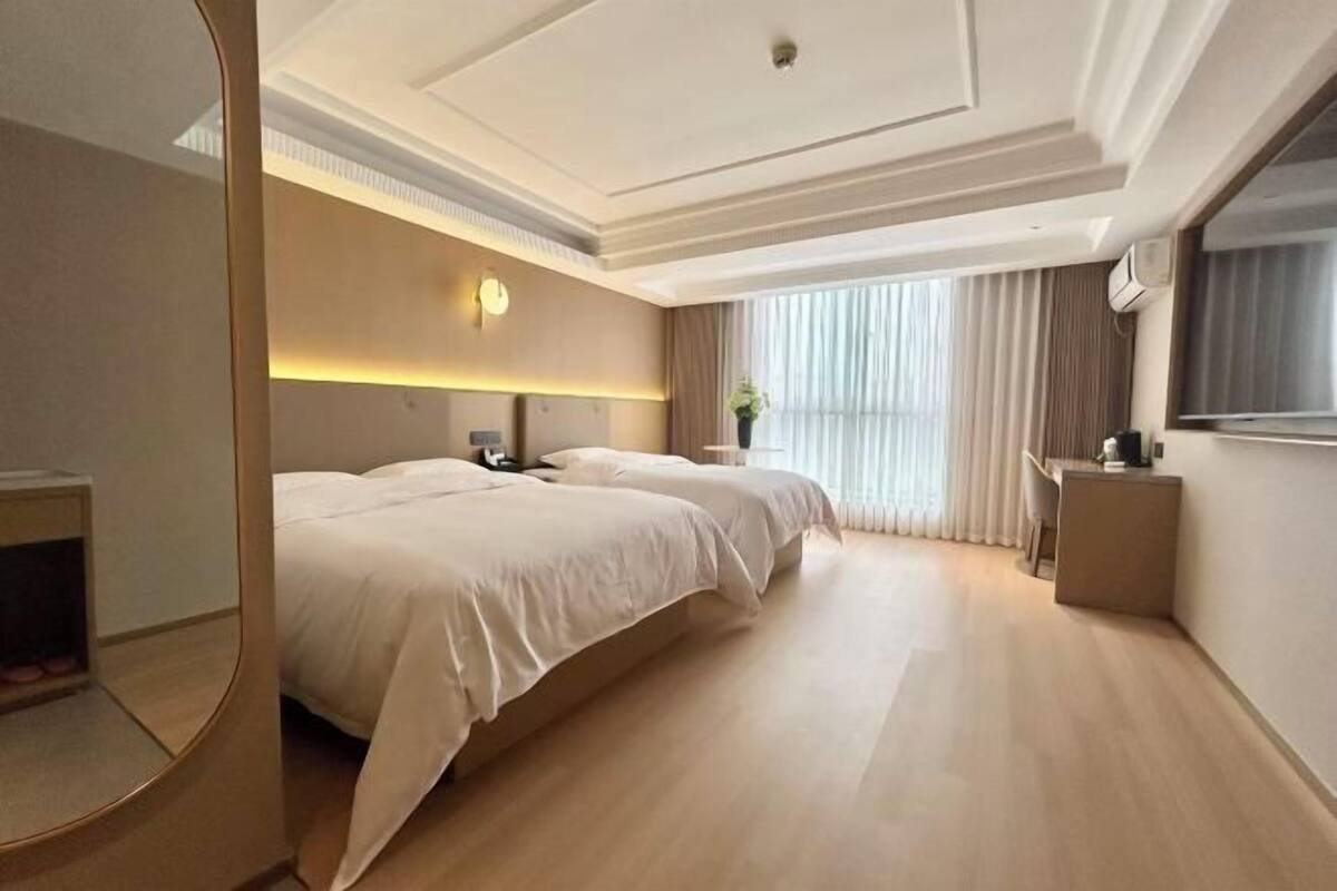 Une chambre d’hôtel avec deux lits, un bureau, un miroir et une grande fenêtre avec des rideaux.