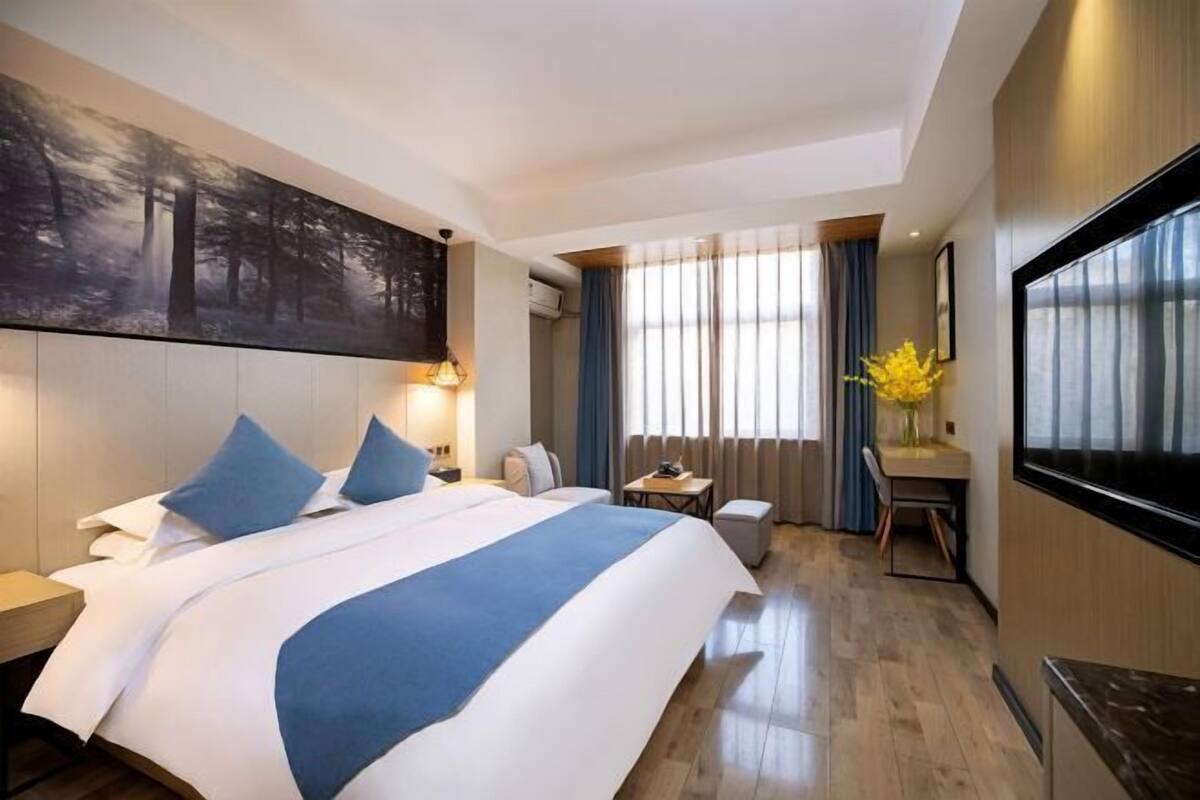 Une chambre d’hôtel avec un grand lit, un bureau, une chaise, une télévision et un tableau au mur.
