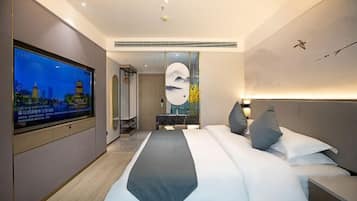 A modern hotel room with a large bed, a TV on the wall, and a painting of mountains.