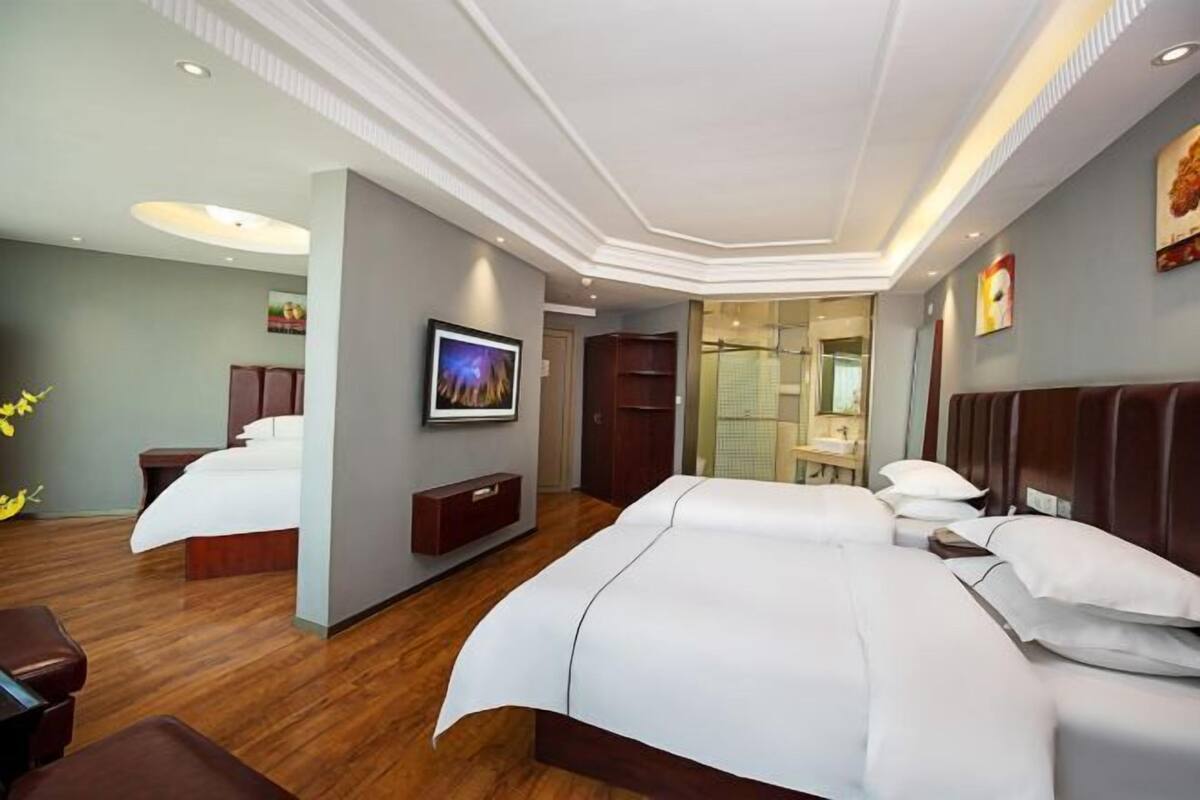 Une chambre d’hôtel avec deux lits, une télévision, une armoire et une salle de bain visible à travers une porte en verre.