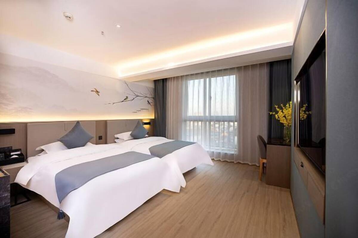 Une chambre d’hôtel moderne, dotée de deux lits, d’une grande fenêtre avec rideaux, d’un téléviseur à écran plat et d’une œuvre d’art accrochée au mur.