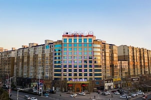 A multi-story hotel with a central entrance, multiple floors, and a parking area in front.
