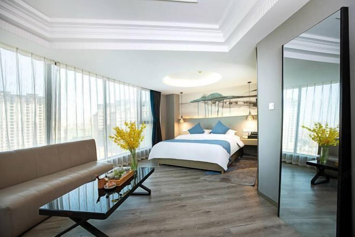 Une chambre d’hôtel moderne avec un grand lit, un canapé, une table à manger et une grande fenêtre avec des rideaux.
