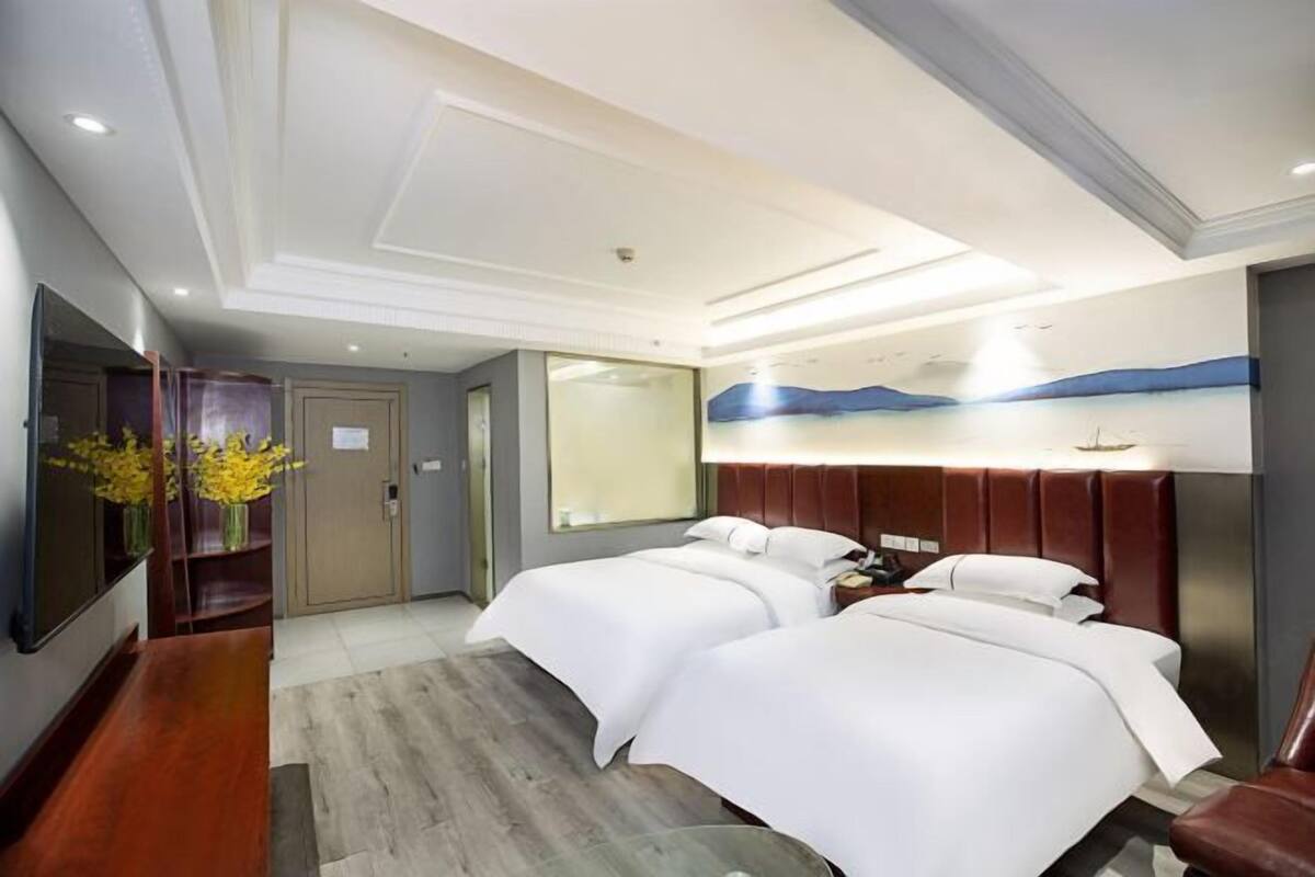Une chambre d’hôtel avec deux lits, un téléviseur à écran plat, un bureau en bois et un vase de fleurs.