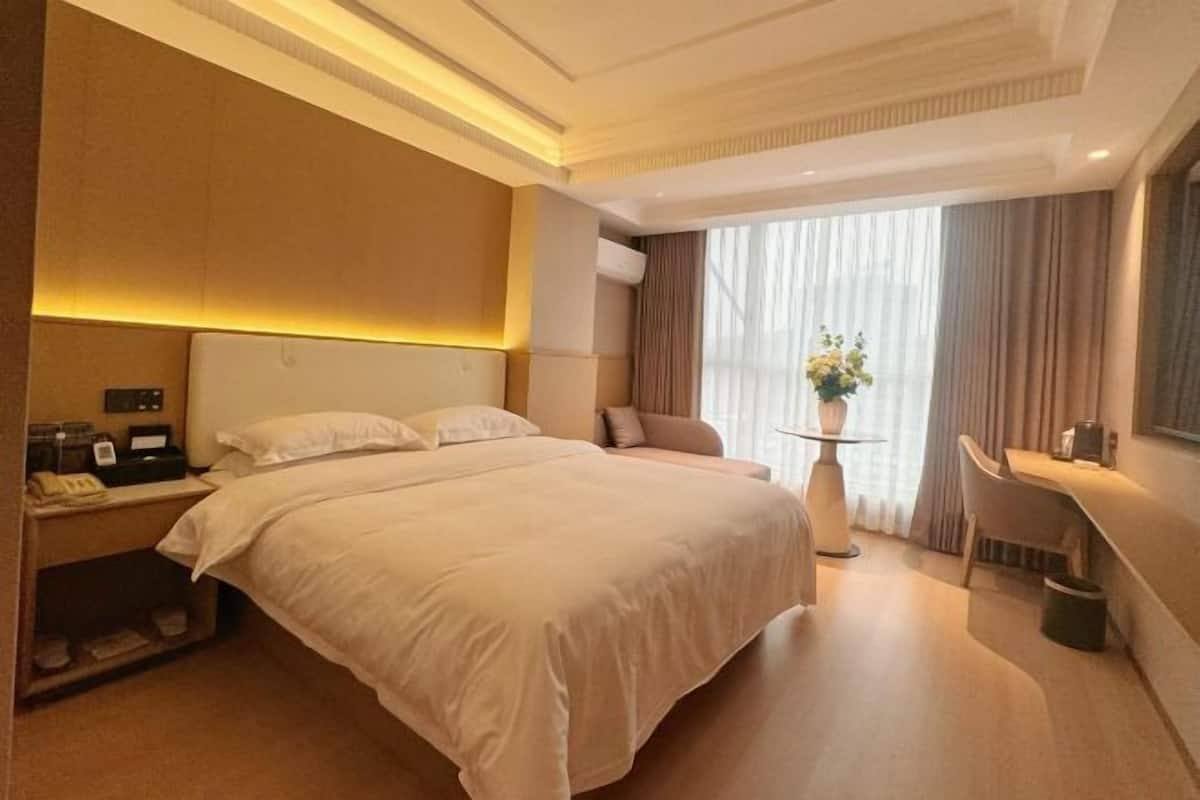 Une chambre d’hôtel moderne, dotée d’un grand lit, d’une table de chevet et d’un petit espace bureau.