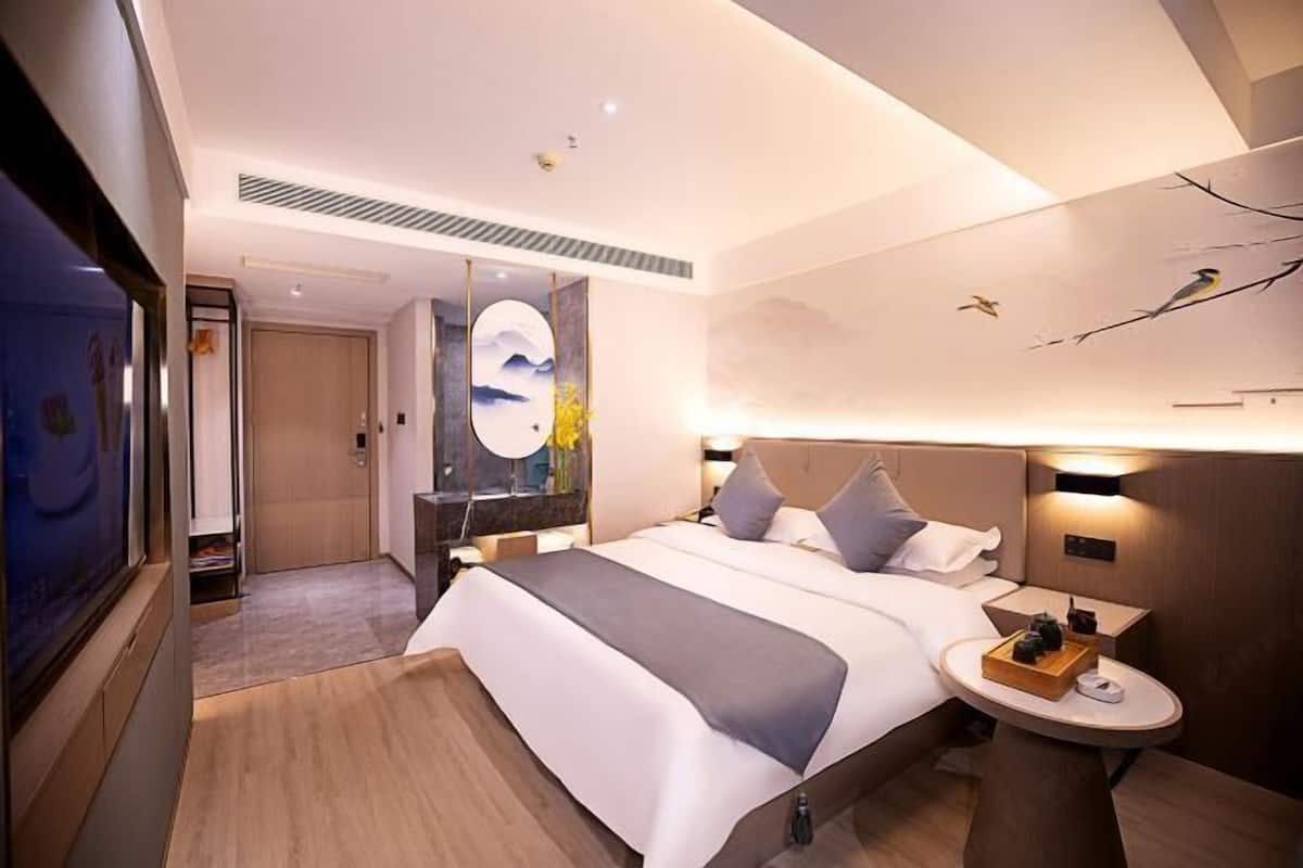 Une chambre d’hôtel moderne avec un grand lit, des tables de chevet, un miroir fixé au mur et une fresque peinte au plafond.