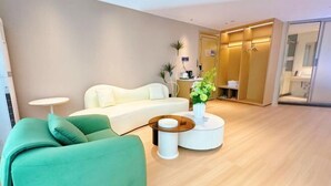 Een moderne hotelkamer met een groene bank, een witte fauteuil, een ronde salontafel en een klein bijzettafeltje.