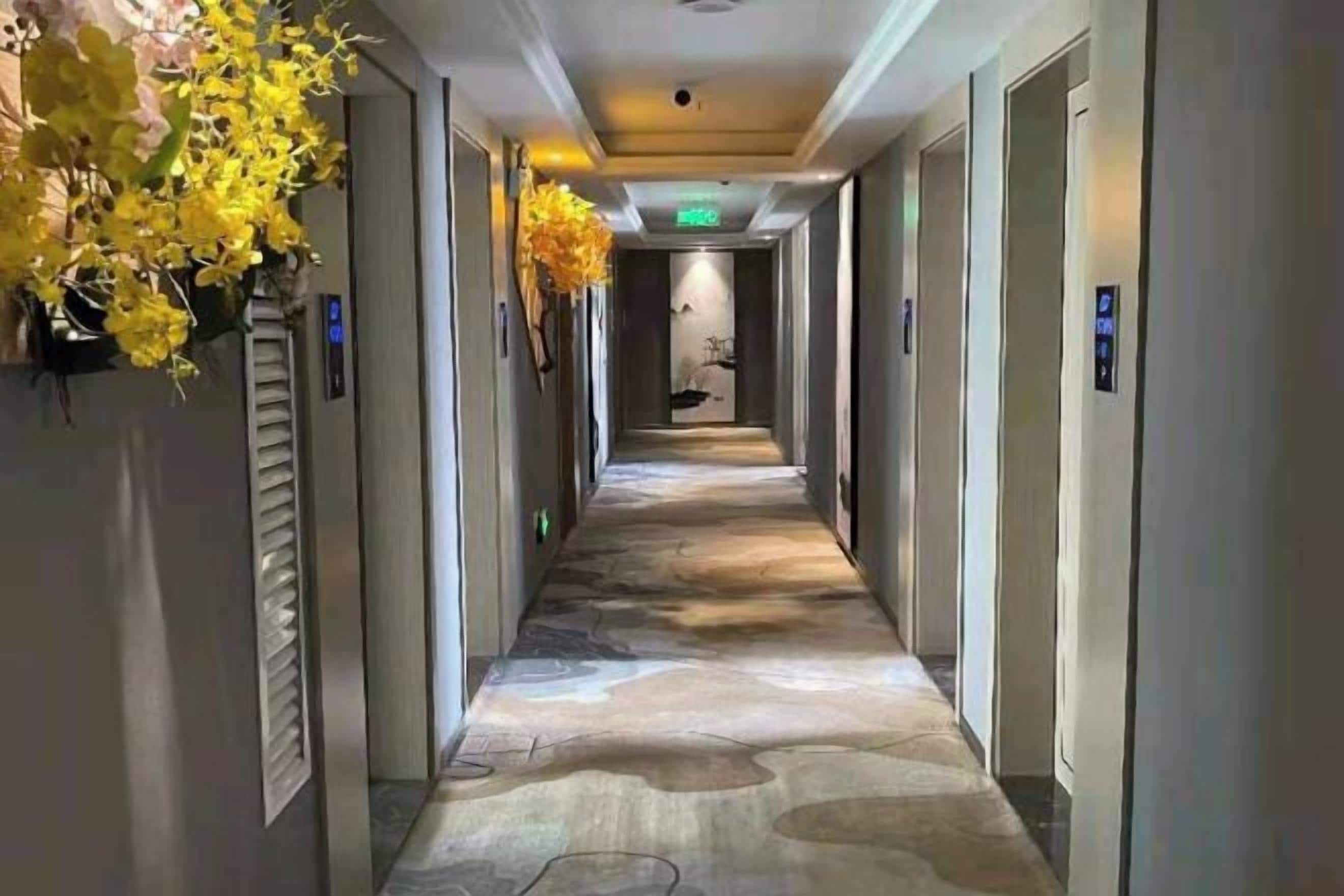 A hotel hallway with a patterned floor, doors on both sides, and a sign indicating the direction to the elevator.