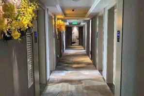 Pasillo de hotel con piso estampado, puertas a ambos lados y un cartel que indica la dirección del ascensor.