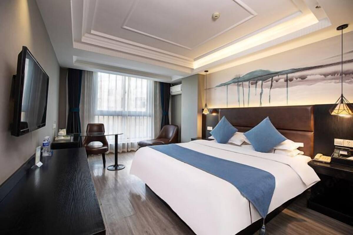 Une chambre d’hôtel avec un grand lit, un bureau, une chaise, une télévision et un tableau au mur.