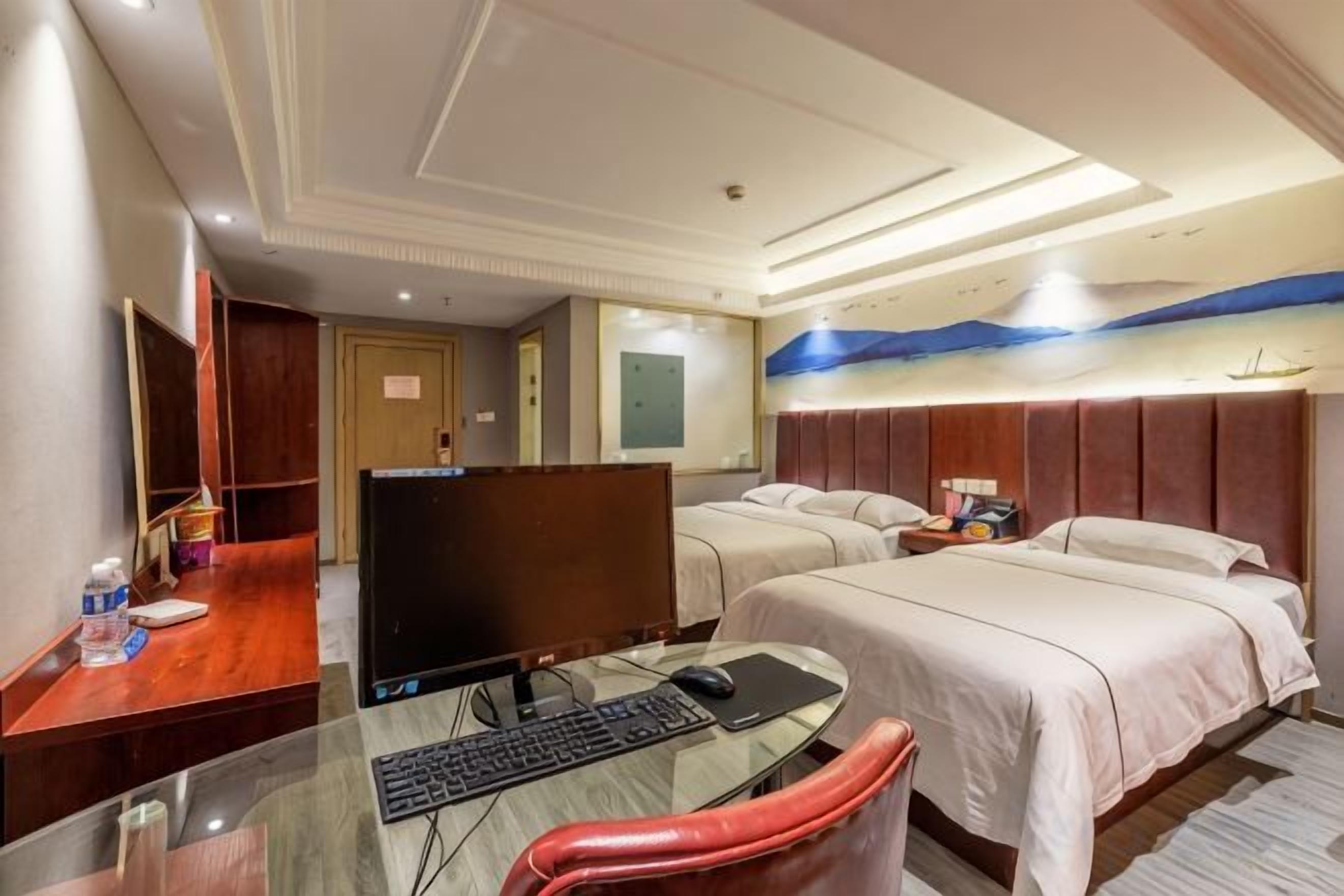 A hotel room with a desk, computer, two beds, and a large window.