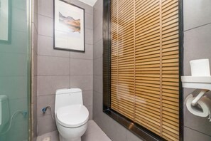 Een moderne badkamer met toilet, een lijst met foto aan de muur, en een raam met houten jaloezieën.