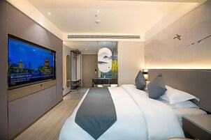 Quarto de hotel moderno com uma cama grande, televisão de tela plana, uma obra de arte na parede e uma mesa de cabeceira.