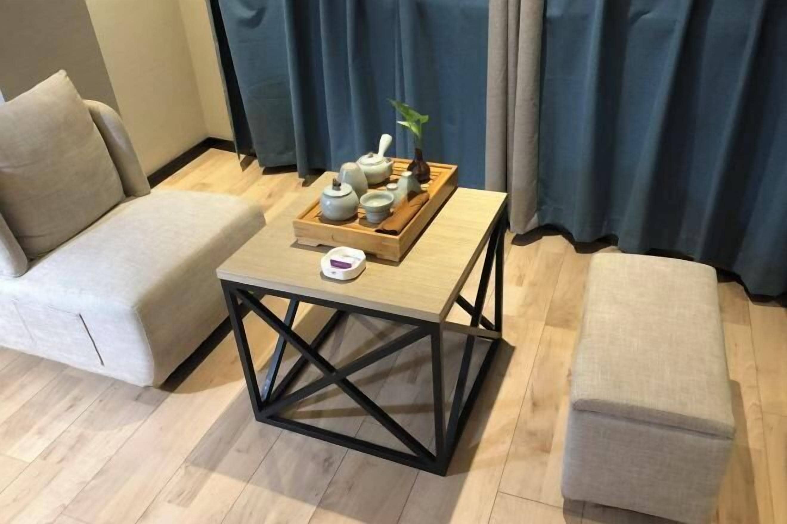 A room with a wooden table, two beige sofas, and a wooden tray with teapots and cups.