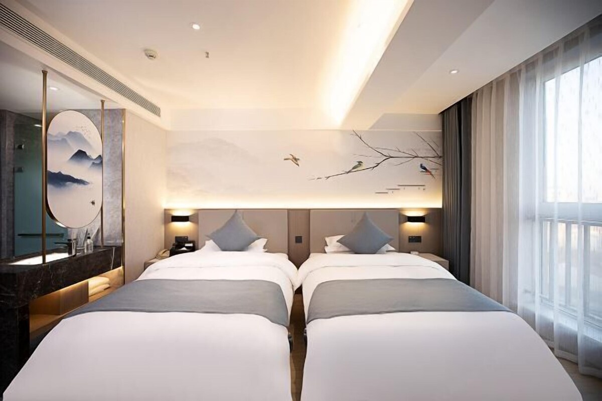 Ein Hotelzimmer mit zwei Betten, einem großen Spiegel, einem Wandbild und einem fenster mit Vorhängen.