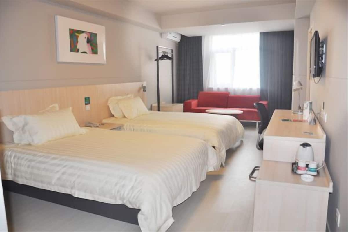 Une chambre d’hôtel avec deux lits, un bureau avec une lampe, un canapé rouge, une télévision et un tableau au mur.