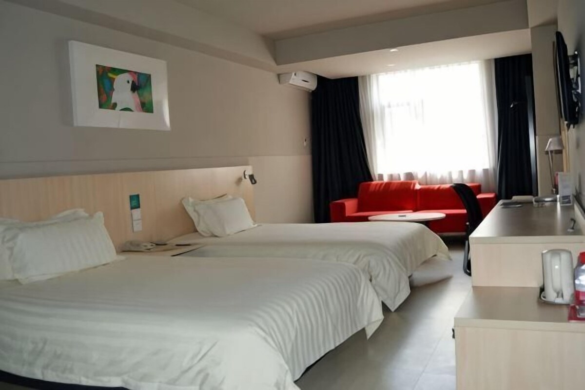Ett hotellrum med två sängar, en röd soffa, ett skrivbord och en tavla på väggen.