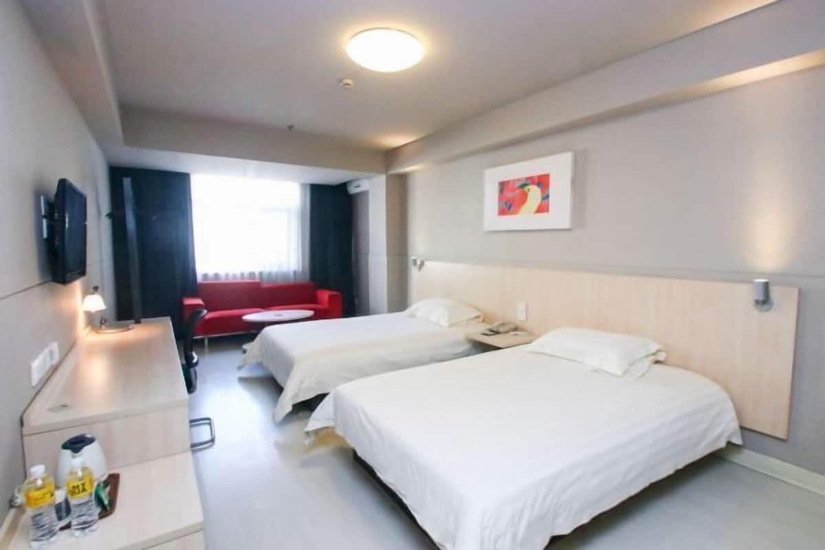 Une chambre d’hôtel avec deux lits, un bureau, une chaise, une télévision et un canapé rouge.