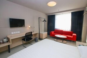 A hotel room with a bed, a desk, a chair, a red sofa, a small table, a TV mounted on the wall, and a window with curtains. - Jinjiang Inn Fuyang Yingshang Road (Fuyang)