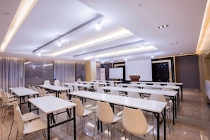 Une salle de conférence équipée de plusieurs tables et chaises, d’un tableau blanc et d’un écran de projection.