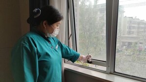 A person in a teal uniform standing by a window, holding a device. - Jinjiang Inn Fuyang Yingshang Road (Fuyang)