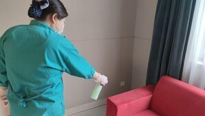 A person in a teal uniform cleaning a red sofa with a spray bottle. - Jinjiang Inn Fuyang Yingshang Road (Fuyang)