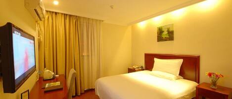 A hotel room with a bed, a desk with a television, a nightstand, and a wall-mounted air conditioner.