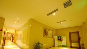 A hotel lobby with a long corridor, a potted plant, a painting, and an elevator. - Greentree Inn Jiangsu Taizhou Jingjiang Bus Statio (Taizhou)