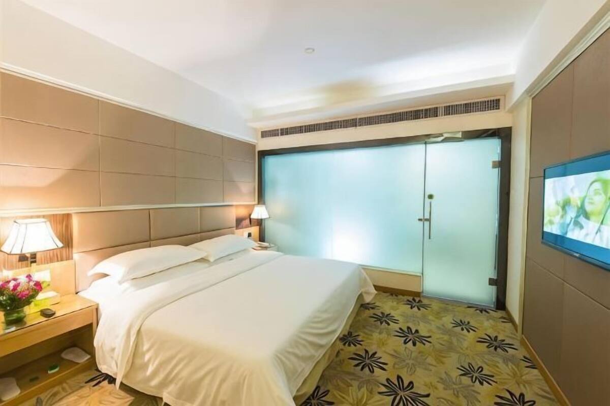 A hotel room with a bed, nightstand, lamp, TV, and a sliding door.